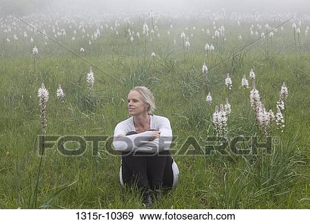 Stock Photo - Italy, Liguria, Woman sitting in green field of wild flowers on foggy day. Fotosearch