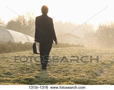 Stock Photograph - Italy, Piedmont, businessman walking in frosty meadow near greenhouses. Fotosearch