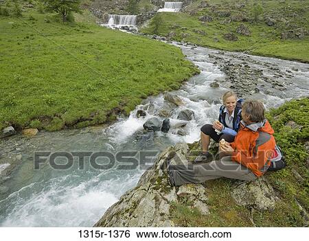 Stock Photograph - Italy, Piedmont, couple having picnic by mountain creek. Fotosearch
