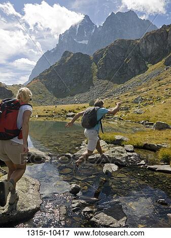 Italy, Piedmont, Couple jumping between rocks along edge of mountain lake View Large Photo Image Stock Photo - Italy, Piedmont, Couple jumping between rocks along edge of mountain lake. Fotosearch