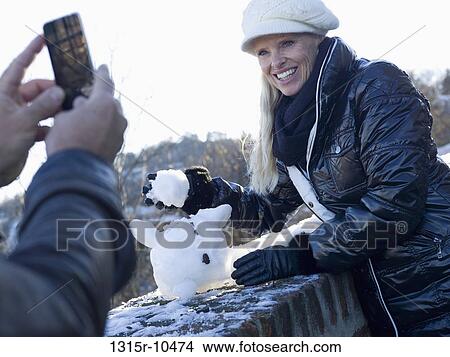 Picture - Italy, Piedmont, Couple taking picture of miniature snowman. Fotosearch