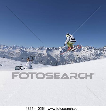 Italy, Piedmont, Jafferau, Teenage skier jumps over snowy ridgecrest, shows off in front of snowboarder View Large Photo Image Stock Image - Italy, Piedmont, Jafferau, Teenage skier jumps over snowy ridgecrest, shows off in front of snowboarder. Fotosearch