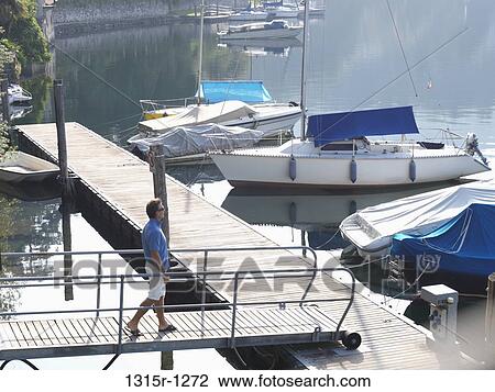 Italy, Piedmont, Lake Orta, Man walking over bridge to sailboat pier View Large Photo Image Stock Image - Italy, Piedmont, Lake Orta, Man walking over bridge to sailboat pier. Fotosearch