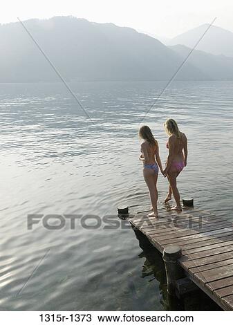 Stock Image - Italy, Piedmont, Lake Orta, Mother and daughter testing water at lake edge. Fotosearch