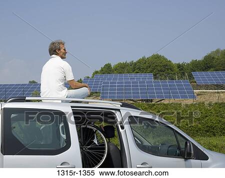 Italy, Piedmont, Man sitting on car roof, looking at solar panels View Large Photo Image Stock Photography - Italy, Piedmont, Man sitting on car roof, looking at solar panels. Fotosearch