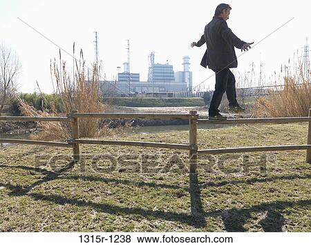 Italy, Piedmont, Man walking along fence post in balance, power plant in background View Large Photo Image Stock Photo - Italy, Piedmont, Man walking along fence post in balance, power plant in background. Fotosearch