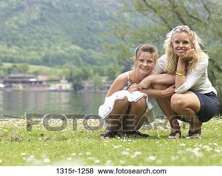 Italy, Piedmont, Mother and daughter crouching in meadow near lake View Large Photo Image Stock Photo - Italy, Piedmont, Mother and daughter crouching in meadow near lake. Fotosearch