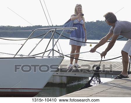 Italy, Piedmont Smiling woman photographing man pulling sailboat into dock View Large Photo Image Stock Image - Italy, Piedmont Smiling woman photographing man pulling sailboat into dock. Fotosearch