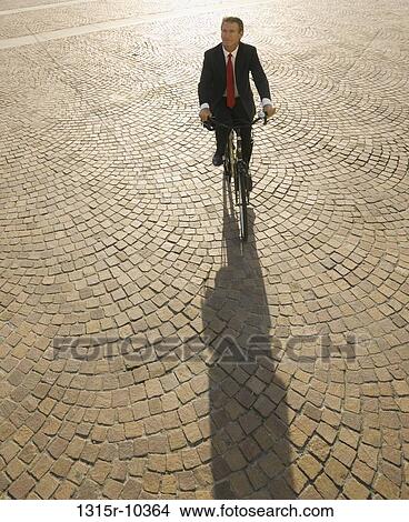 Picture - Italy, Piedmont, Turin, Businessman cycling across cobblestone piazza. Fotosearch