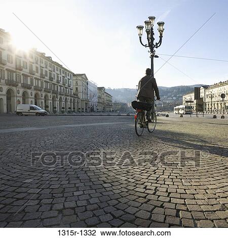 Stock Image - Italy, Piedmont, Turin, Businessman cycling across plaza. Fotosearch