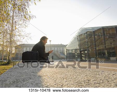 Italy, Piedmont, Turin, Businessman sitting on stone wall, sending text message View Large Photo Image Stock Photo - Italy, Piedmont, Turin, Businessman sitting on stone wall, sending text message. Fotosearch