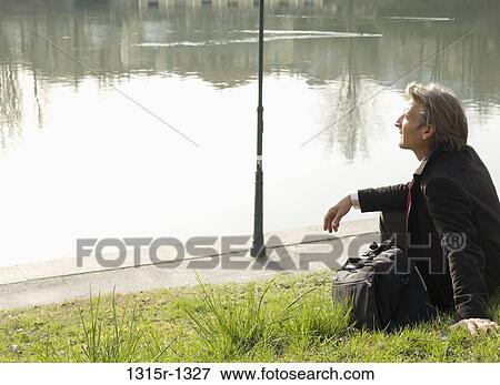 Italy, Piedmont, Turin, Businessman sitting on lawn by river View Large Photo Image Stock Photo - Italy, Piedmont, Turin, Businessman sitting on lawn by river. Fotosearch