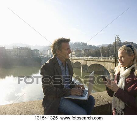 Stock Photography - Italy, Piedmont, Turin, couple with laptop and phone on bridge. Fotosearch