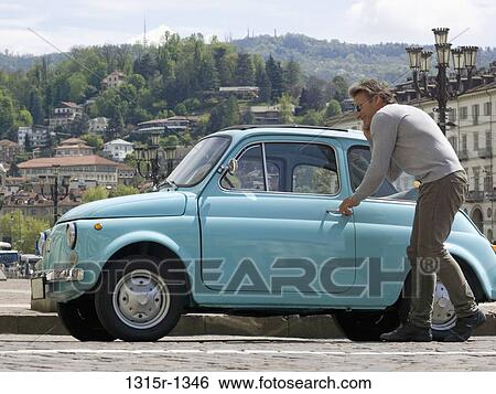Stock Photograph - Italy, Piedmont, Turin, man entering vintage car. Fotosearch