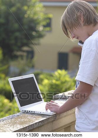 Italy, Piedmont, Turin, teenage boy working on laptop and talking on cell phone on terrace View Large Photo Image Stock Image - Italy, Piedmont, Turin, teenage boy working on laptop and talking on cell phone on terrace. Fotosearch