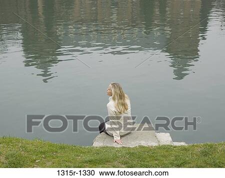 Stock Image - Italy, Piedmont, Turin, woman sitting on edge of river. Fotosearch