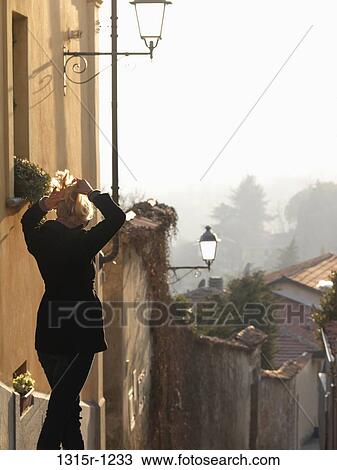 Italy, Piedmont, Woman adjusting hair while walking down medieval street View Large Photo Image Stock Image - Italy, Piedmont, Woman adjusting hair while walking down medieval street. Fotosearch