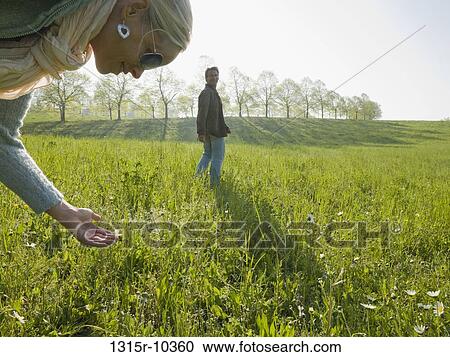 Italy, Piedmont, Woman looking at flower in meadow, man in background View Large Photo Image Stock Image - Italy, Piedmont, Woman looking at flower in meadow, man in background. Fotosearch