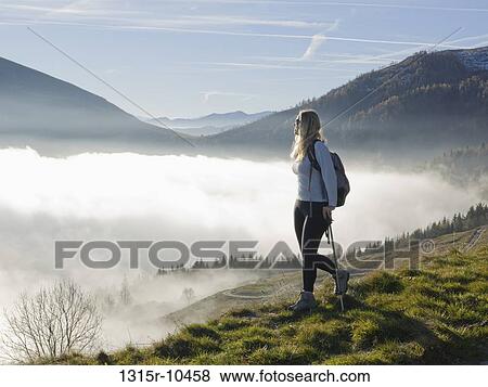Stock Photo - Italy, Piedmont, Woman looking at mountains from meadow above fog. Fotosearch