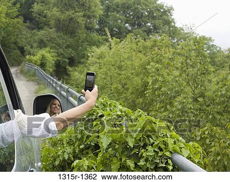 Stock Image - Italy, Piedmont, Woman taking cell phone picture of green forest. Fotosearch