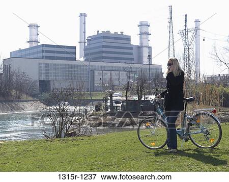 Stock Photo - Italy, Piedmont, Woman with bike on park, near electrical power plant in winter's day. Fotosearch