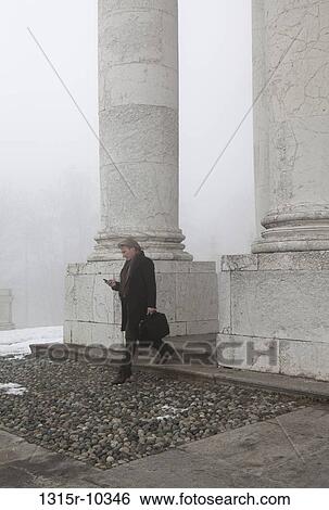 Italy, Turin, Businessman checking text message while stepping between marble pillars View Large Photo Image Stock Photograph - Italy, Turin, Businessman checking text message while stepping between marble pillars. Fotosearch