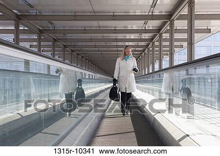 Stock Image - Italy, Turin, Woman checking text message on moving walkway. Fotosearch