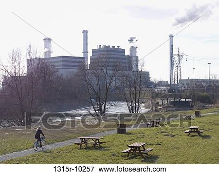 Italy, Woman bicycles through park past gas fired electrical plant View Large Photo Image Stock Photo - Italy, Woman bicycles through park past gas fired electrical plant. Fotosearch