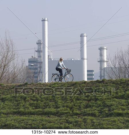 Italy, Woman bikes along raised dike near gas fired electrical plant View Large Photo Image Picture - Italy, Woman bikes along raised dike near gas fired electrical plant. Fotosearch
