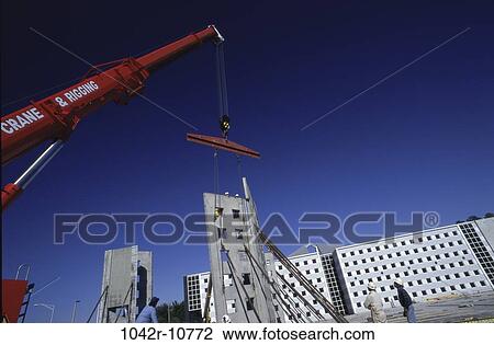 Stock Image - Low angle view of a crane carrying a section of a building. Fotosearch