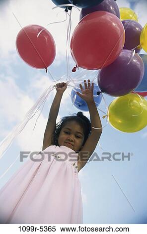 Stock Photography - Low angle view of a girl holding balloons. Fotosearch