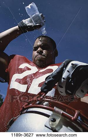 Stock Photo - Low angle view of an American football player pouring water on his head. Fotosearch