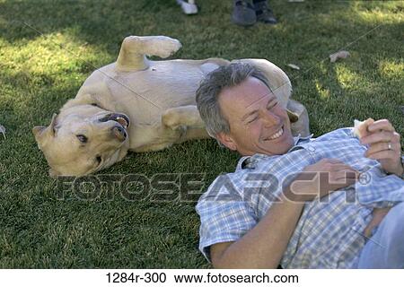 Stock Image - Man lying on a lawn with his dog. Fotosearch