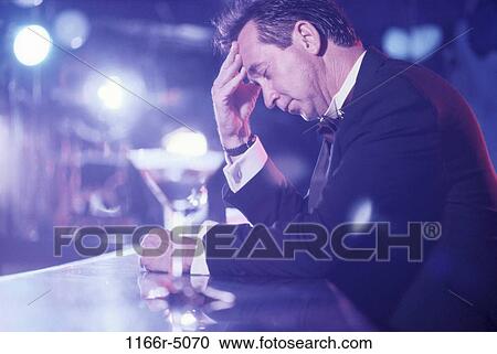 Stock Image - Man sitting at a bar holding his head. Fotosearch