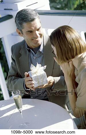 Stock Image - Mid adult man holding a gift sitting outdoors with a woman. Fotosearch