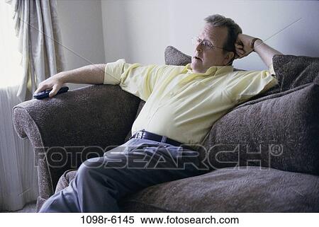Mid adult man sitting on a couch watching television View Large Photo Image Stock Photography - Mid adult man sitting on a couch watching television. Fotosearch