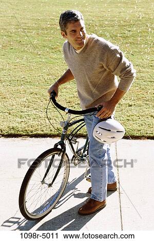 Stock Image - Mid adult man standing with a bicycle. Fotosearch