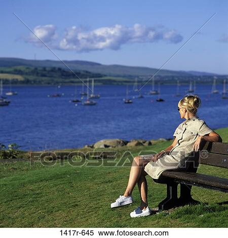 Stock Photography - Mid adult woman sitting on a bench looking at a lake. Fotosearch