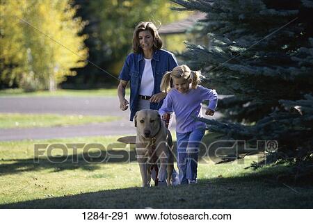 Stock Image - Mother and daughter walking with their pet dog on a lawn. Fotosearch