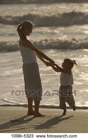 Stock Image - Mother and her daughter holding hands at the beach. Fotosearch