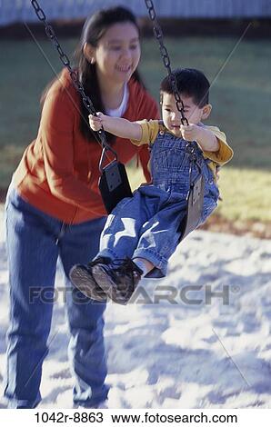 Stock Image - Mother pushing son on a swing. Fotosearch