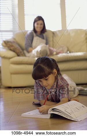 Mother sitting on a couch looking at her daughter studying on the floor View Large Photo Image Picture - Mother sitting on a couch looking at her daughter studying on the floor. Fotosearch