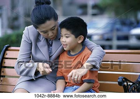 Stock Image - Mother sitting on a park bench with her son. Fotosearch