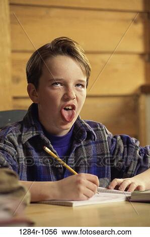 Stock Photograph - Portrait of a boy seated at a desk in front of a book making a face. Fotosearch