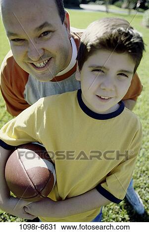 Stock Image - Portrait of a father and son playing American football. Fotosearch