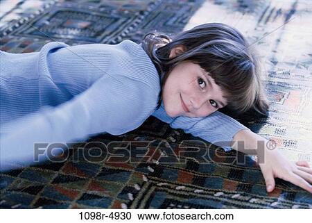Stock Image - Portrait of a girl lying down on a rug. Fotosearch