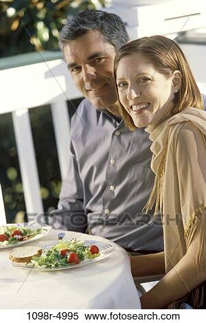 Stock Photography - Portrait of a mid adult couple sitting at a table outdoors. Fotosearch
