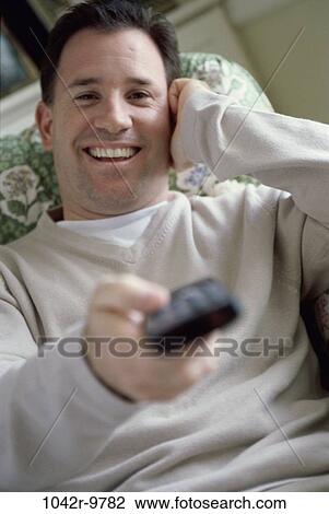 Stock Image - Portrait of a mid adult man holding a remote control. Fotosearch