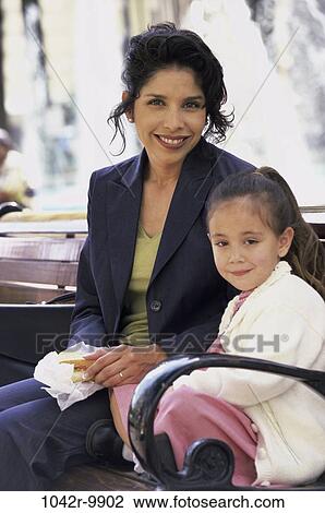 Stock Image - Portrait of a mother and daughter sitting on a park bench. Fotosearch