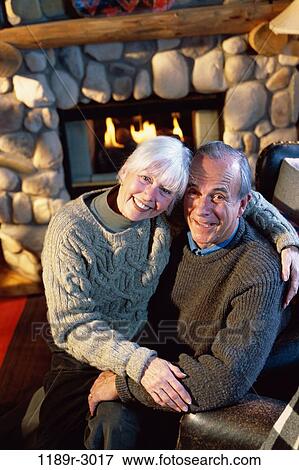 Stock Photo - Portrait of a senior couple hugging in front of a fireplace. Fotosearch